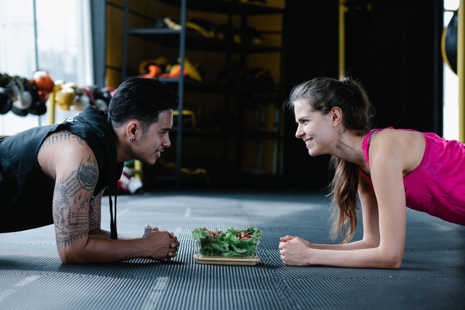 Two people holding a plank face to face over a bowl of fresh salad