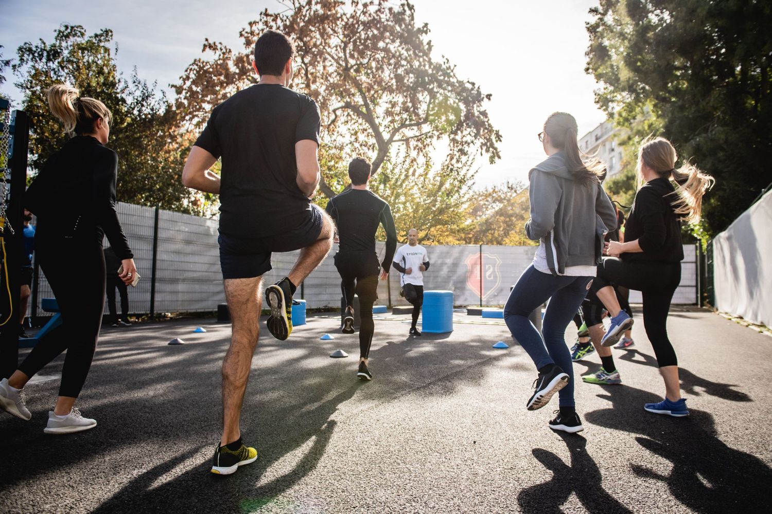 A group of coworkers doing a high-knee warm-up together outdoors with a trainer